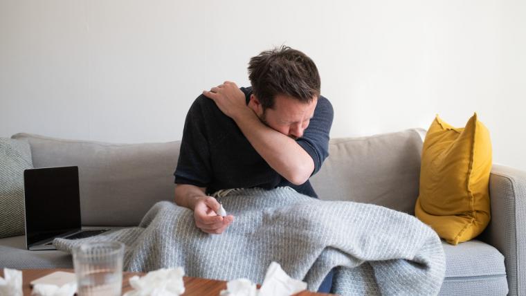 Man sitter i en soffa och nyser pga förkylning