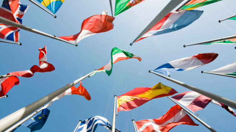 En rad europeiska flaggor på flaggstänger fotograferade underifrån